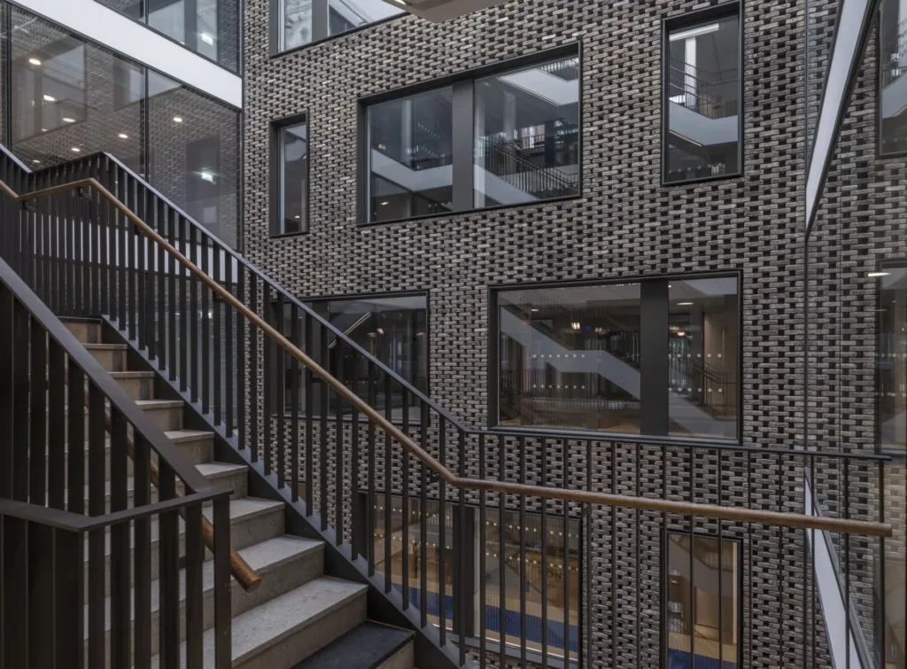 Trappa med metallräcken och tegelvägg med stora fönster som reflekterar insidan av byggnaden.