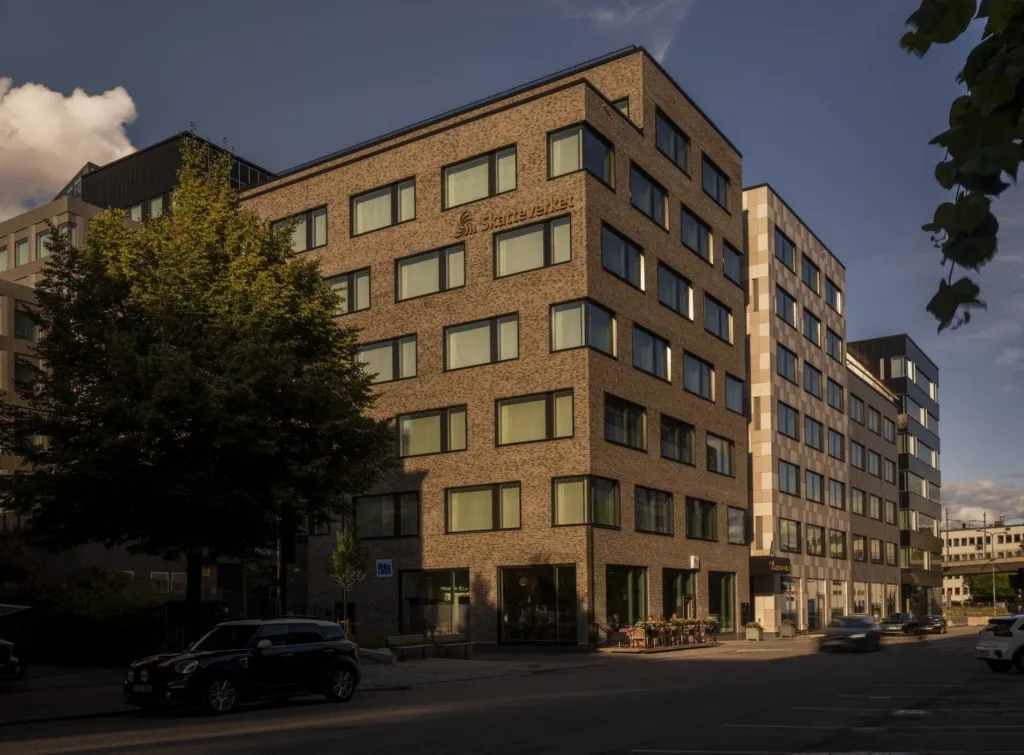 En byggnad med brun tegel- och glasfasad, belägen vid en trädbevuxen gata i ett stadsområde.
