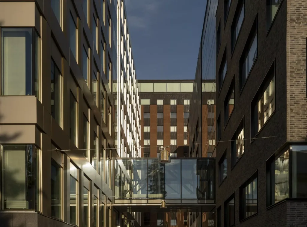 En smal passage mellan två höga byggnader, med en glasbro som förbinder dem under blå himmel.