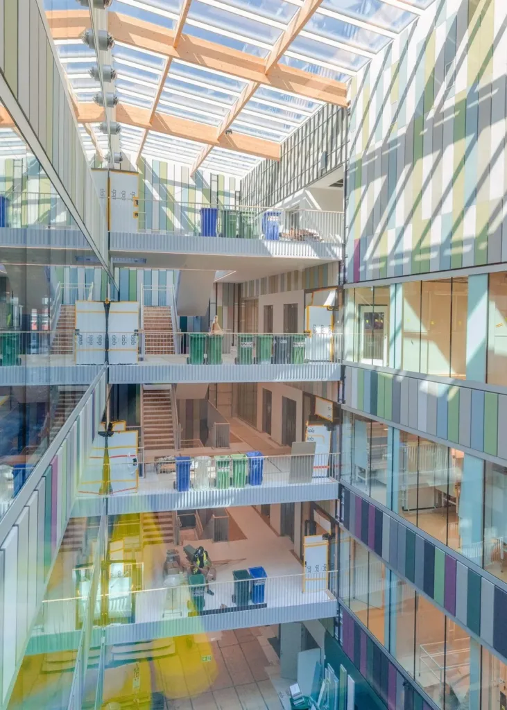 Ett modernt atrium med glasväggar och flera våningar, belyst av naturligt ljus från ett takfönster.