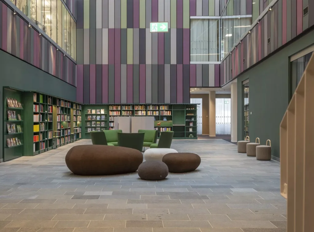 Ett bibliotek med färgglada väggpaneler, gröna möbler och stenliknande sittpuffar på golvet.