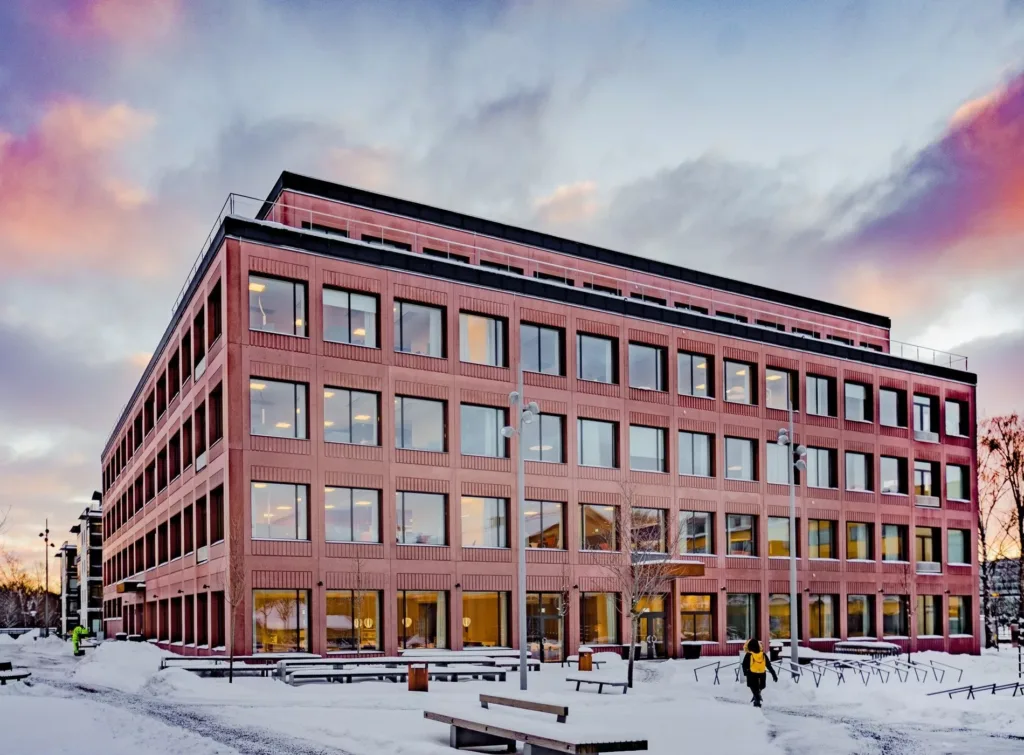 5. En stor tegelbyggnad med många fönster, omgiven av snö och en person som går.