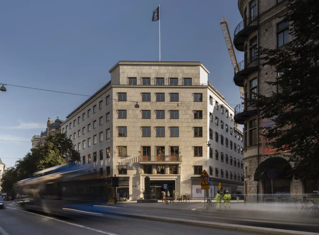 En stor byggnad med klassisk arkitektur och en flagga på taket, med en spårvagn som passerar framför.