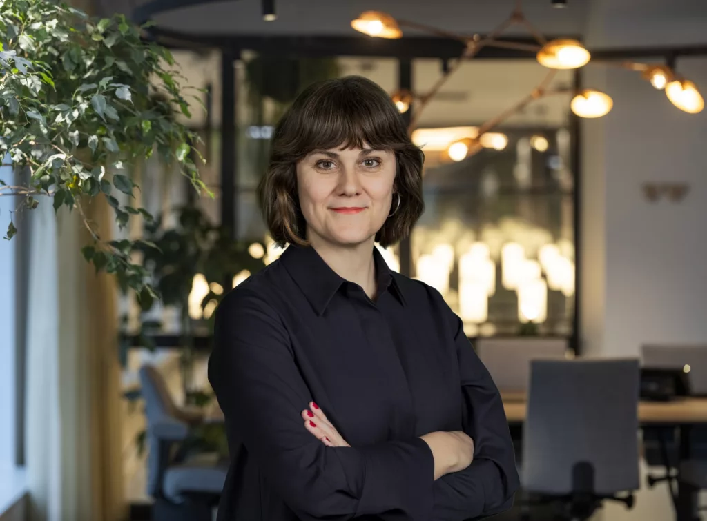 2. En kvinna med mörkt hår och svart skjorta står med armarna i kors i en modern kontorsmiljö.