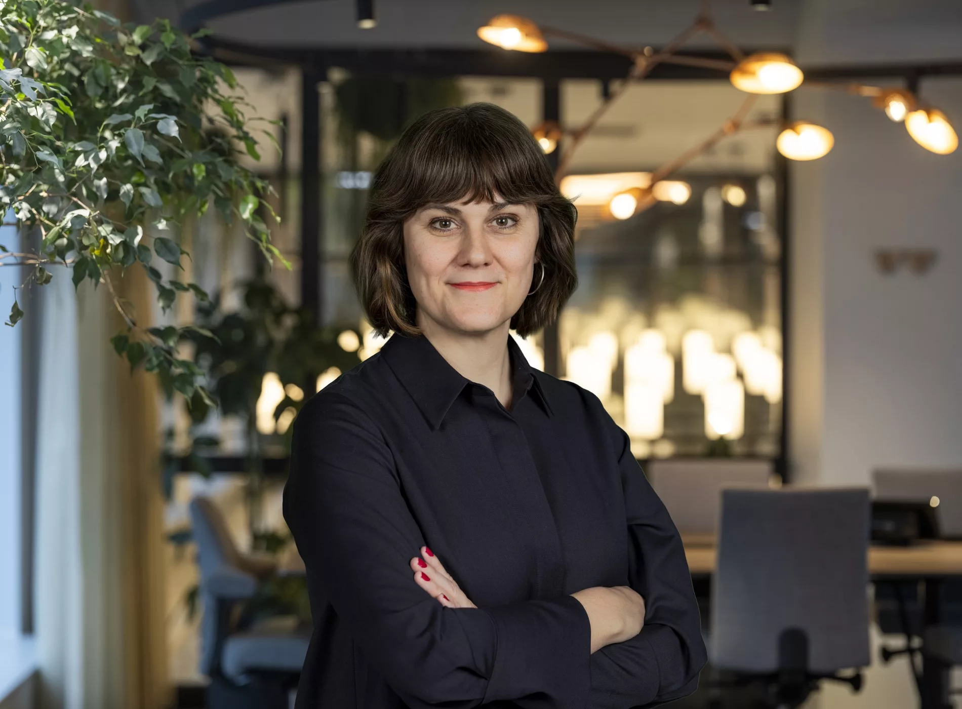 2. En kvinna med mörkt hår och svart skjorta står med armarna i kors i en modern kontorsmiljö.