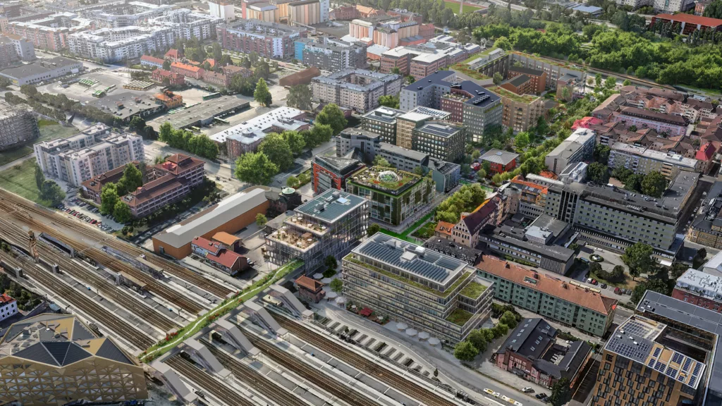 Ett flygfoto över en stadsdel med järnvägsspår, byggnader och grönområden.