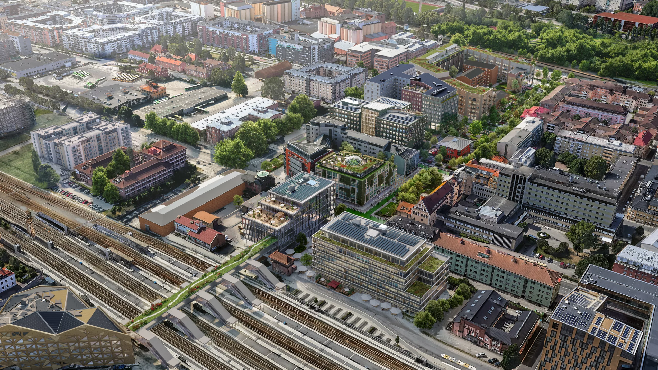 Ett flygfoto över en stadsdel med järnvägsspår, byggnader och grönområden.