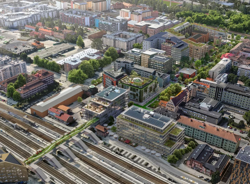 Ett flygfoto över en stadsdel med järnvägsspår, byggnader och grönområden.
