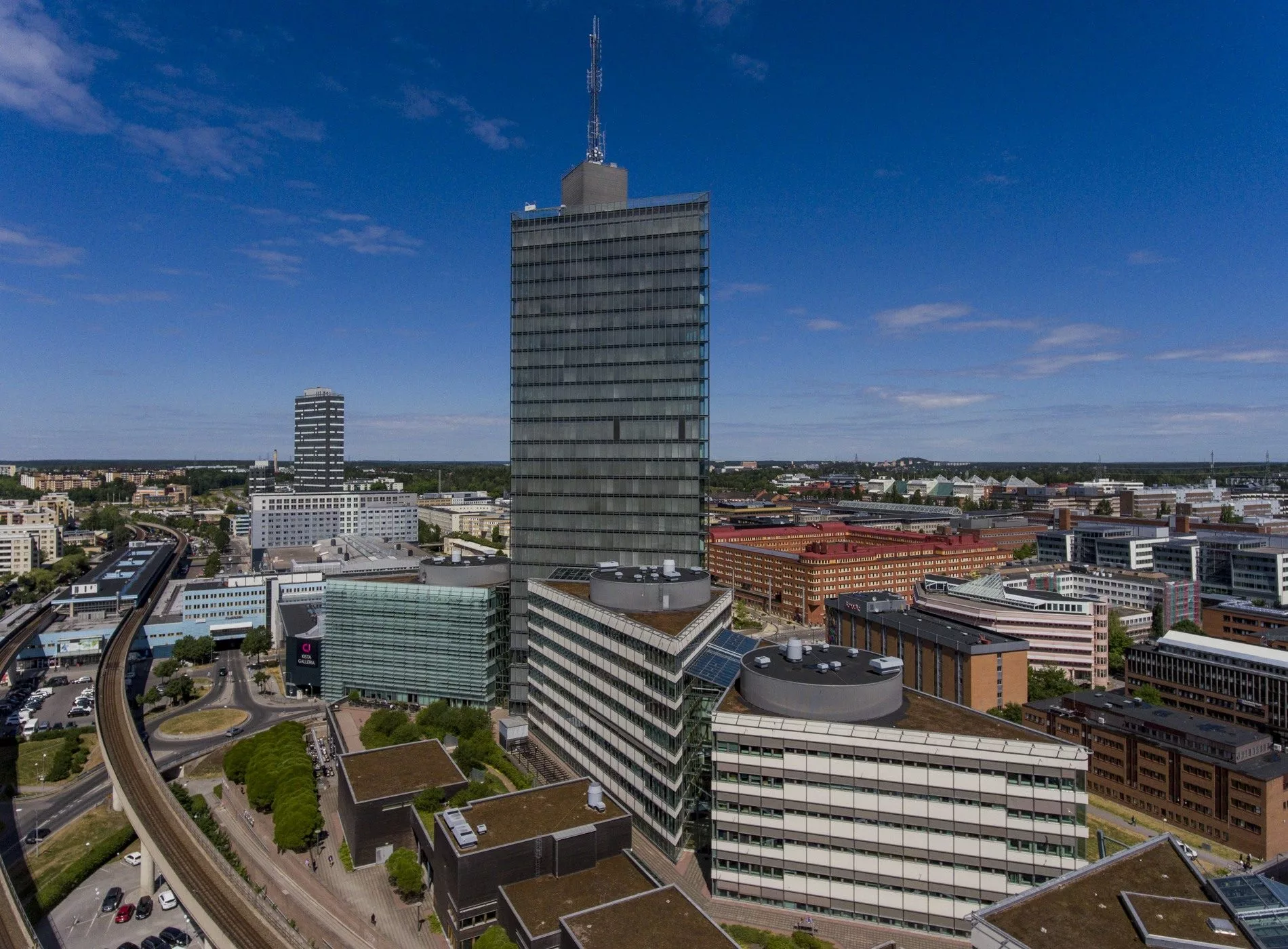 Ett höghus och flera byggnader i stadsmiljö under en klarblå himmel.