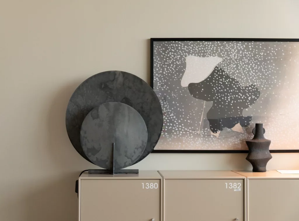 En dekorativ svart skulptur placerad på ett skåp, med en abstrakt tavla hängande ovanför.
