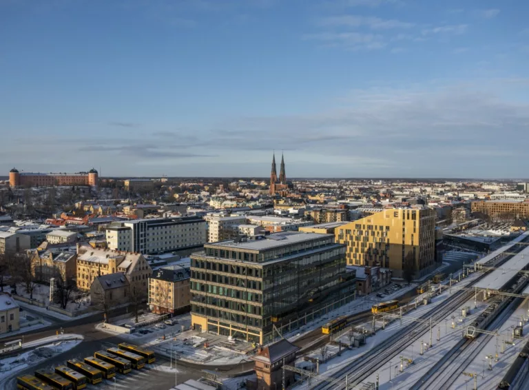 Uppsala stad i vintertid med snötäckta byggnader, kyrktorn i bakgrunden och järnvägsspår i förgrunden.