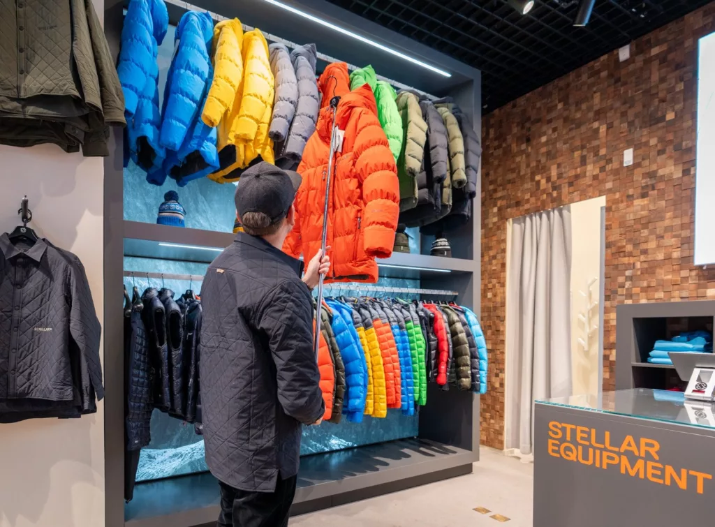 En person i mörk jacka tittar på en hylla fylld med färgglada dunjackor i en butik.