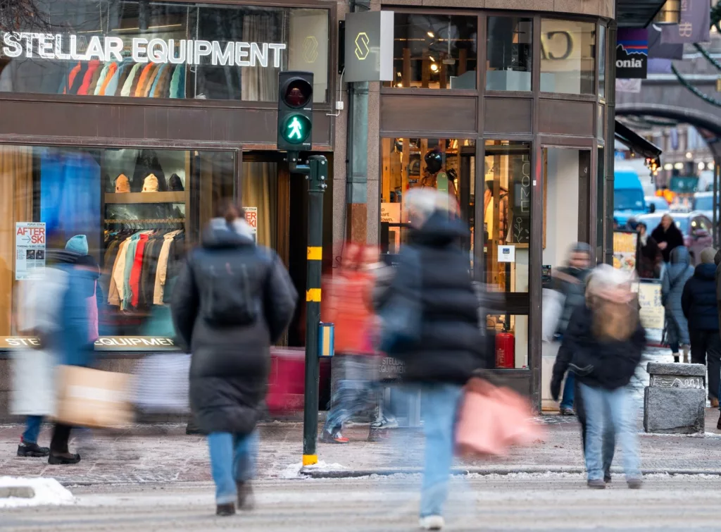 En butiksgata med människor som går förbi och ett skyltfönster med texten "Outdoor Equipment".