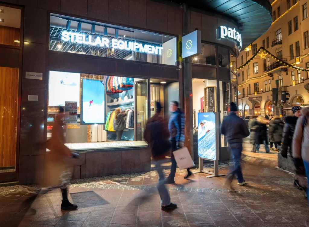 Exteriör av en Stellar Equipment-butik på kvällen, med människor som går förbi och skyltar som lyser.