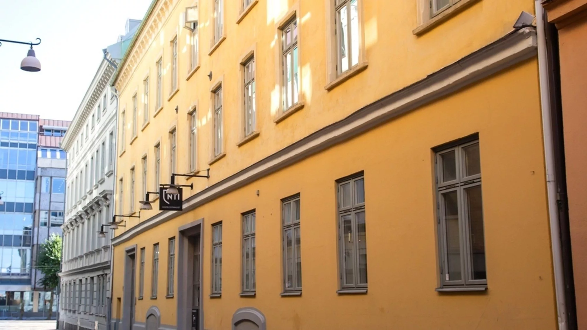 En gul byggnad med flera fönster längs en smal gata, dagsljus lyser på fasaden.