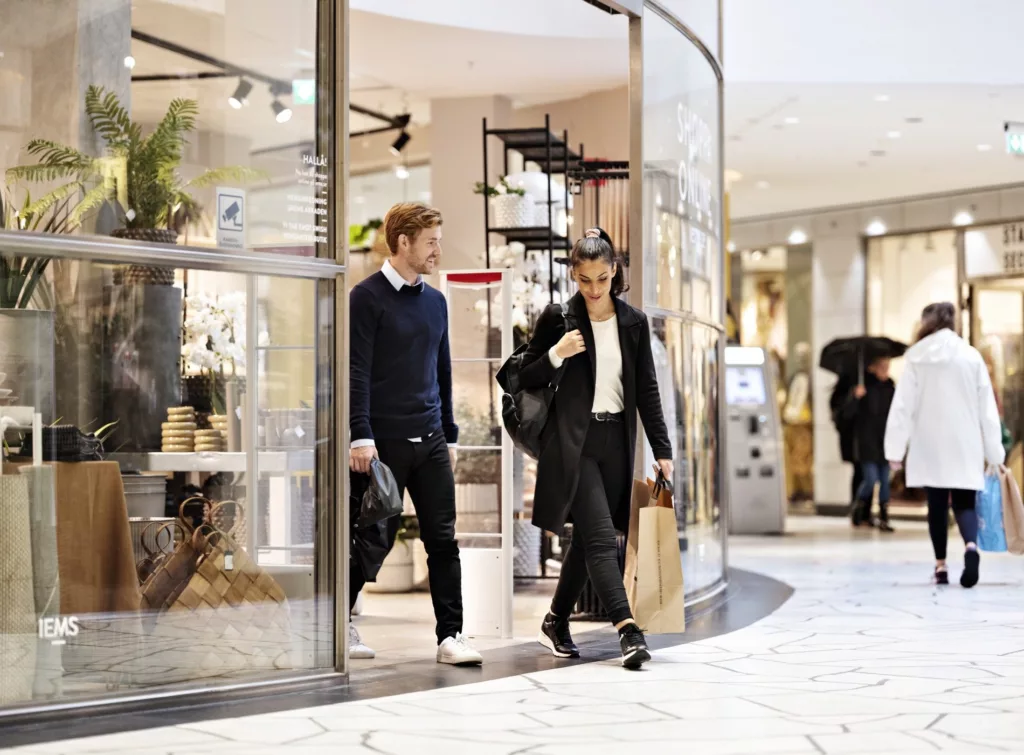 Två personer går ut från en butik i ett köpcentrum, bärandes på shoppingpåsar.