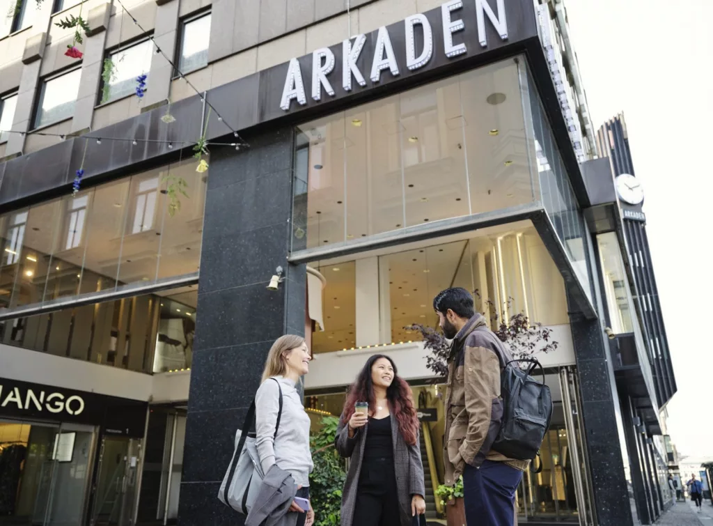 Tre personer står och samtalar framför en byggnad med skylten "Arkaden".