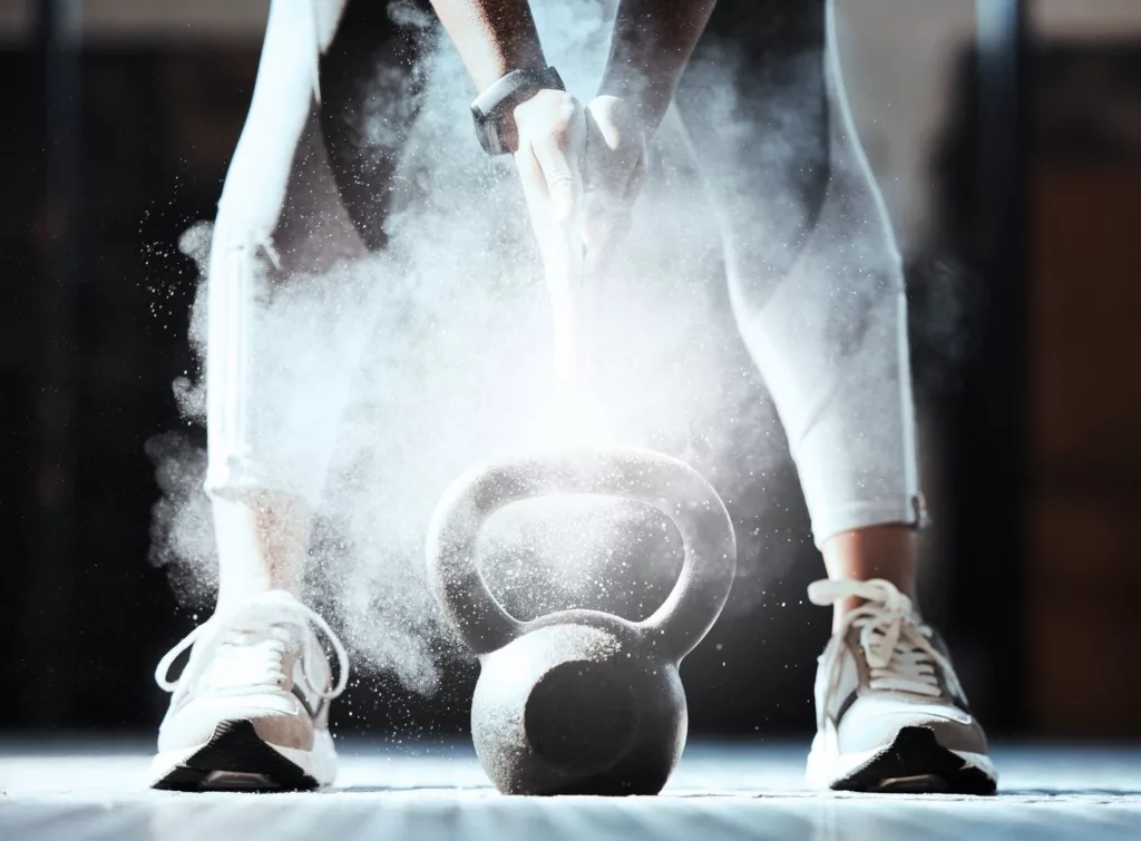 En person i träningstights står med en kettlebell, omgiven av dammande krita.