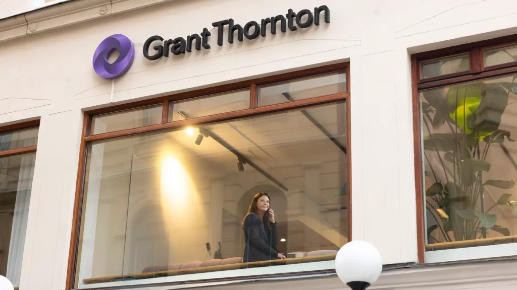 Skyltfönster med texten "Grant Thornton" och en kvinna synlig genom glaset inifrån kontoret.