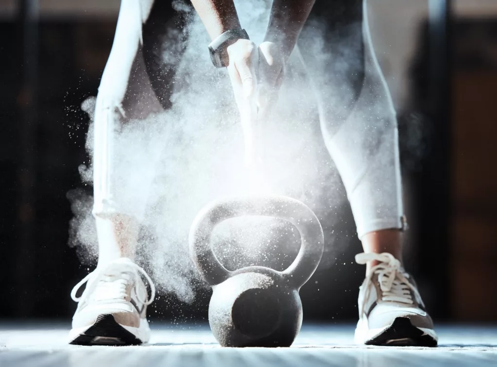 En person i träningskläder som lyfter en kettlebell med kritdamm som sprids i luften.