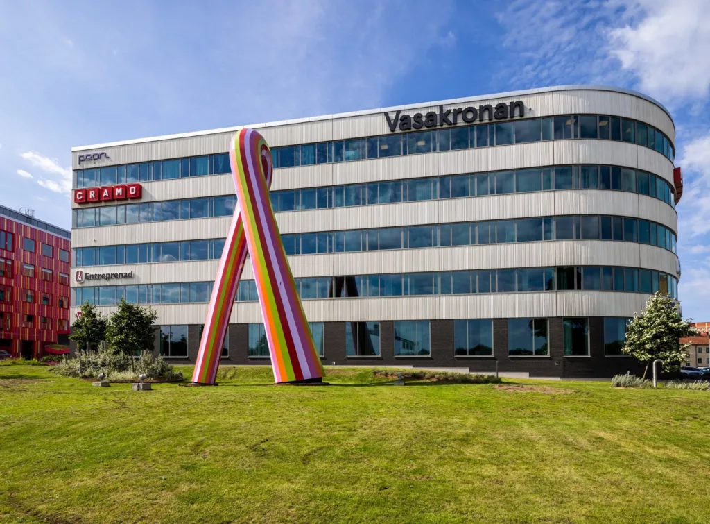 En kontorsbyggnad med texten "Vasakronan" på fasaden och en färgglad skulptur placerad på en gräsmatta framför byggnaden.
