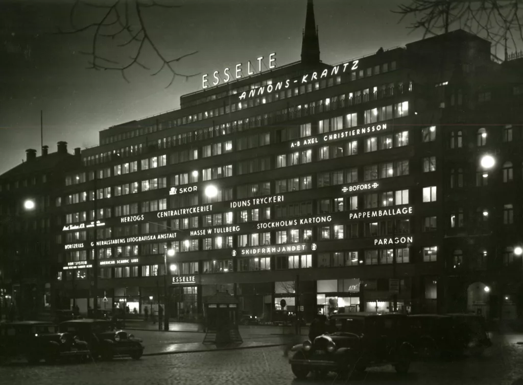 Historisk bild av fastigheten Uggleborg i nattmörker med neonskyltar över hela fasaden.