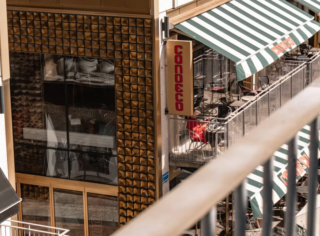 5. Utsikt mot en byggnad med ett skylt med texten "Goodco" och randiga markiser ovanför restaurangmöbler.
