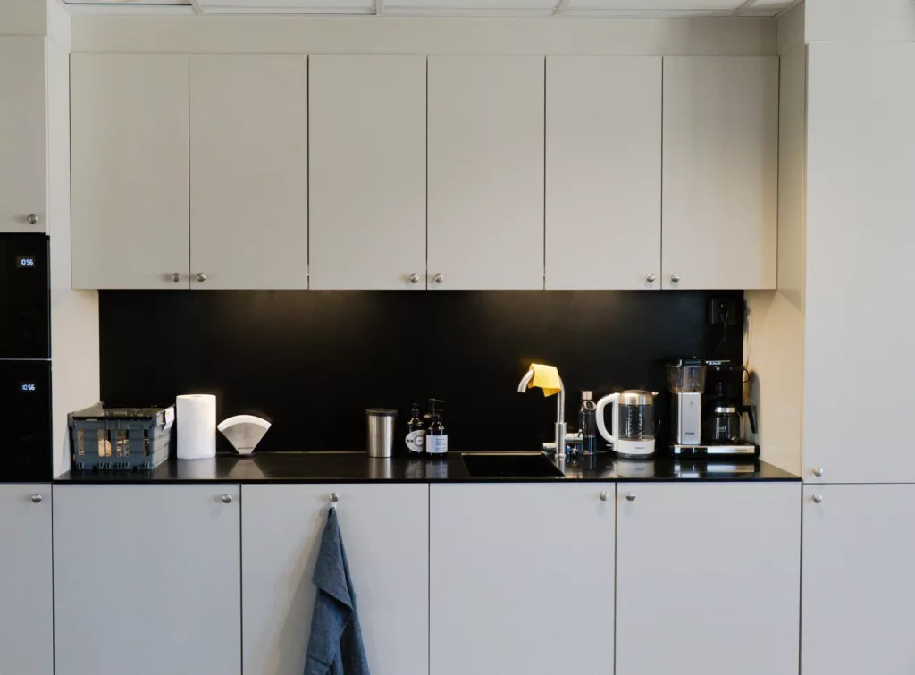 1. En modern köksinredning med vita skåp, svart bänkskiva och köksartiklar, inklusive en vattenkokare och kaffebryggare. En blå kökshandduk hänger på ett skåp.