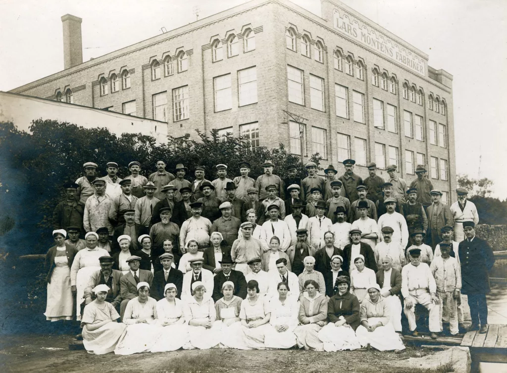 Svartvit bild av fabrikspersonal framför en fabrik i början av 1900-talet.