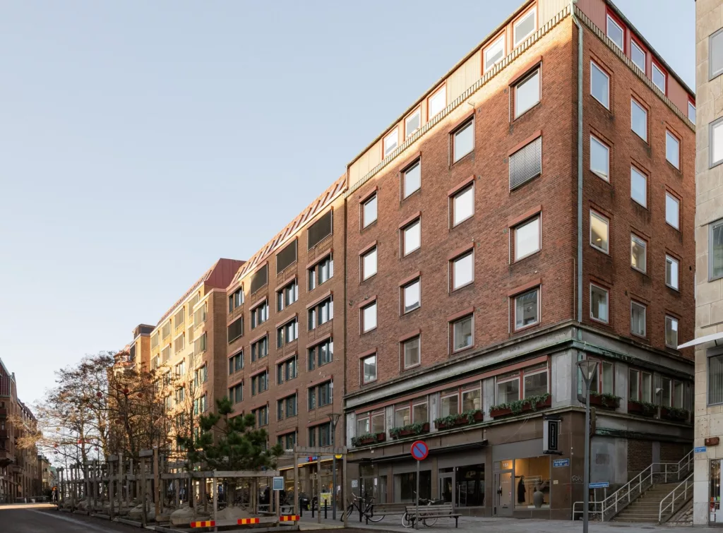 En rad tegelbyggnader i stadsmiljö med flera våningar och stora fönster.