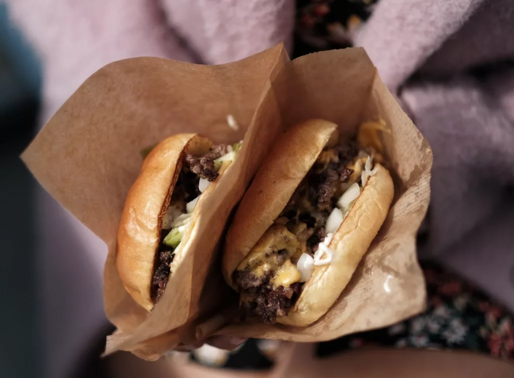 Två hamburgare i brunt papper, fyllda med kött, ost och grönsaker.