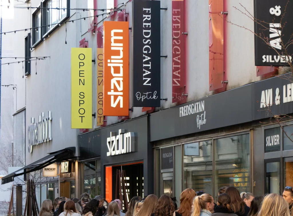 Flera butiksfasader med skyltar, inklusive "Open Spot", "Fredsgatan" och "Stadium".