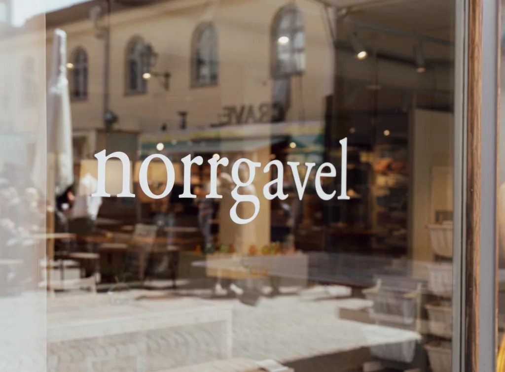 Butiksfönster med texten "norrgavel" tryckt på glaset och en suddig interiör i bakgrunden.