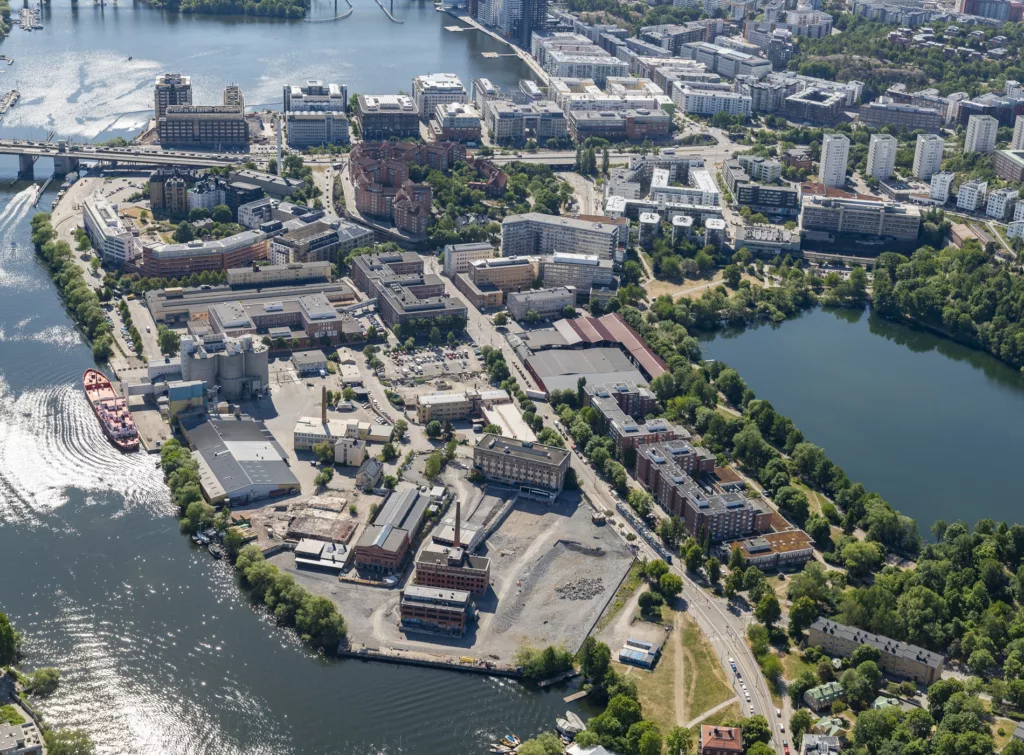 2. Flygbild över ett stadsområde med byggnader, vatten och grönområden.