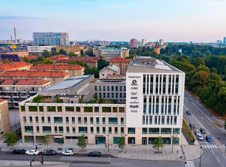 4. En modern byggnad med vita och glasdetaljer, omgiven av gröna träd och omgivande stadsbebyggelse.
