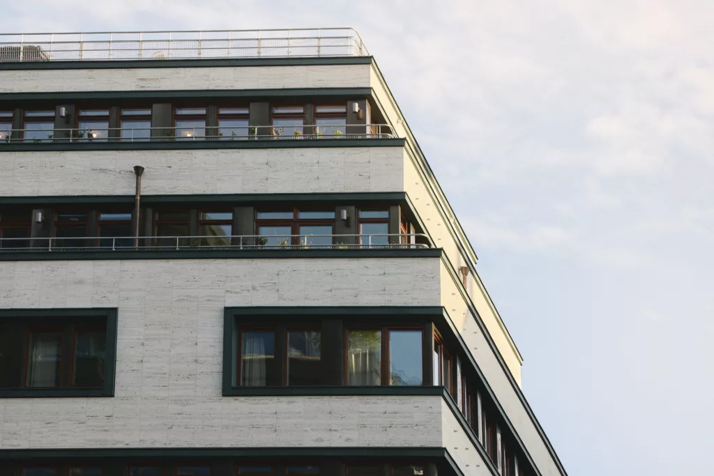 1. Vit byggnad med flera våningar och gröna fönsterkarmar, mot en ljus himmel.