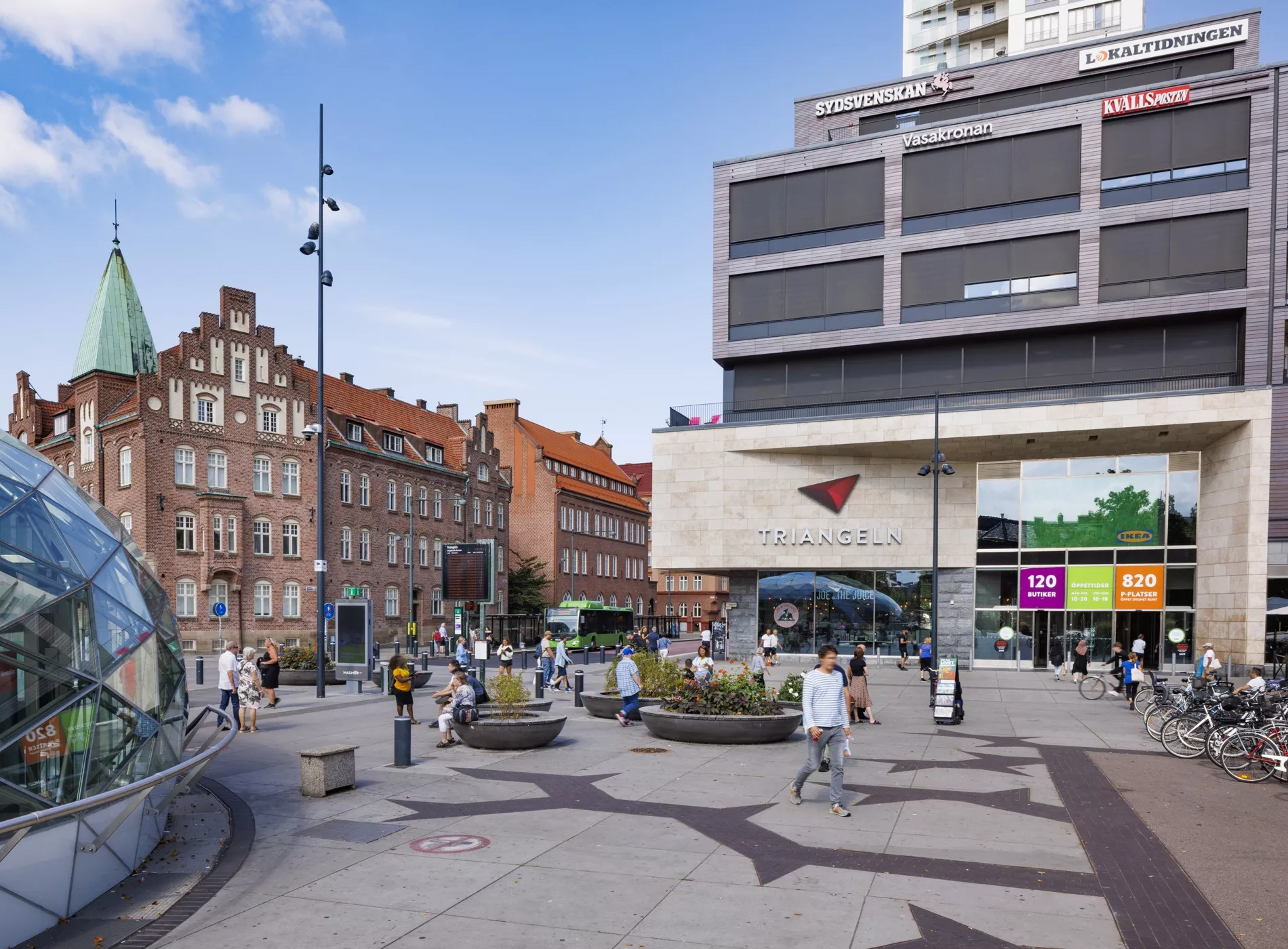 4. En livlig stadsmiljö med människor, byggnader, och ett köpcenter med skyltar och affärer.