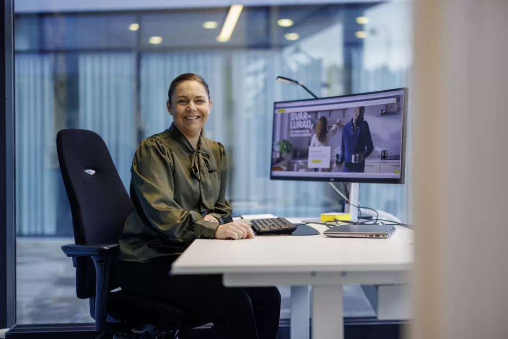 2. En kvinna sitter vid ett skrivbord med en datorskärm som visar ett videomöte.