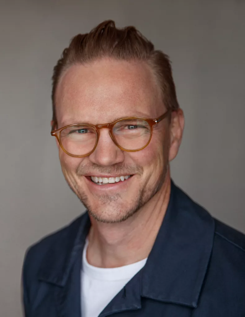 En man med glasögon och kort hår ler mot kameran.