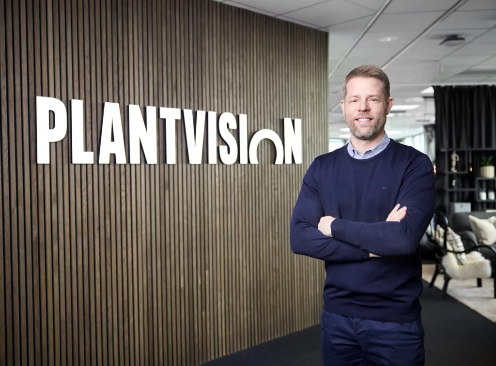 En man står leende framför en vägg med texten "Plantvision" och har armarna i kors.