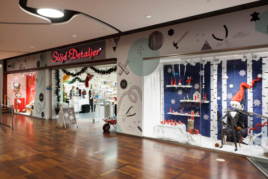 En butik med ett juldekorerat skyltfönster och en röd neonskylt med texten "Sigt Detaljer".