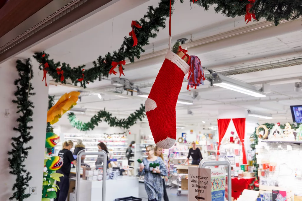 En stor röd julstrumpa hänger från taket i en dekorerad butik.