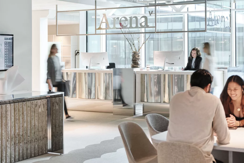Receptionen på Arena med två receptionister bakom disken och människor som rör sig i rummet.