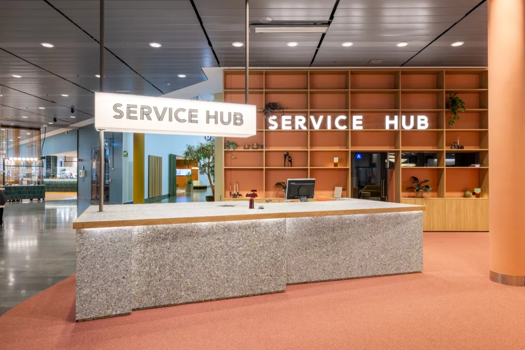 En receptionsdisk med texten "SERVICE HUB" på ljusskyltar, omgiven av träpaneler och moderna detaljer.