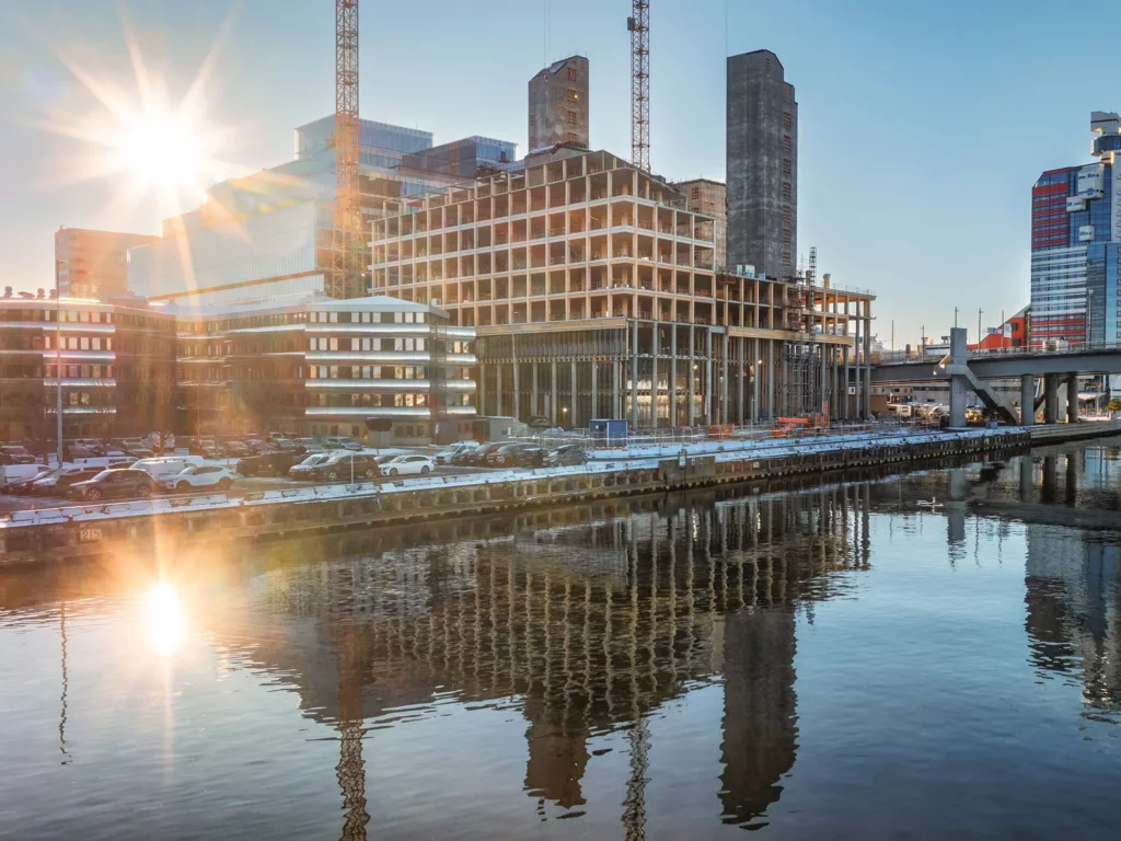 1. En byggarbetsplats med höga byggnader, solens ljus reflekteras i en stilla vattenyta.