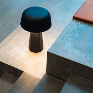 3. En liten bordslampa med svart skärm lyser på en betongyta nära trappsteg.