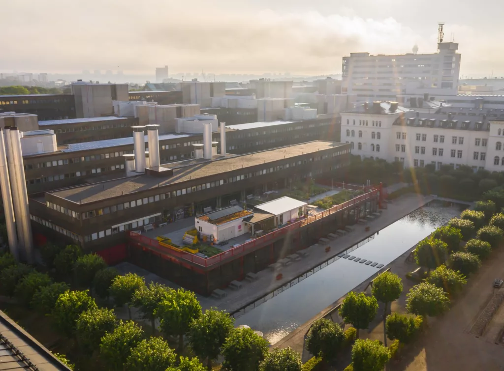 En översiktsbild över en modern byggnad med en innergård, träd och en vattenkanal, omgiven av andra byggnader.
