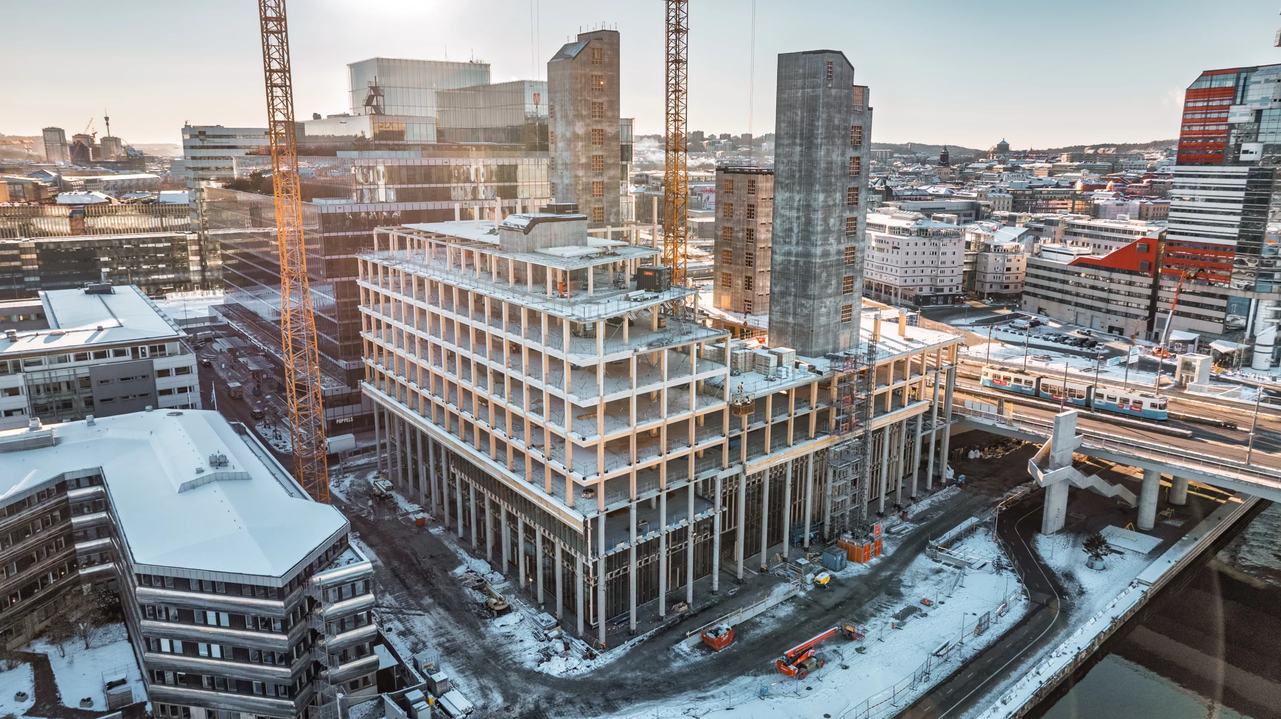 En byggarbetsplats med en stor byggnad under konstruktion, omgiven av snö och kranar.