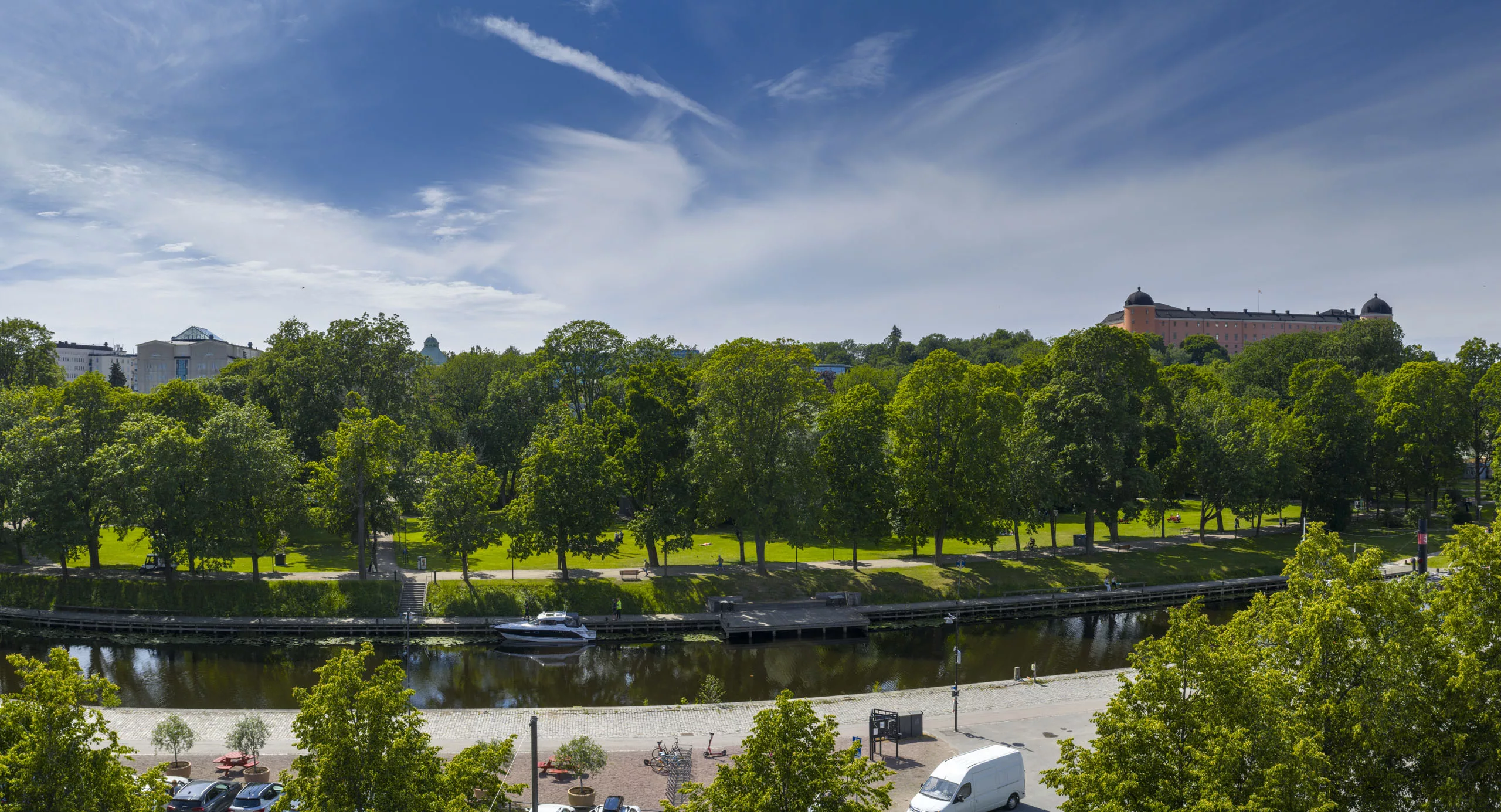 En park med träd och en kanal med båtar under en klarblå himmel.