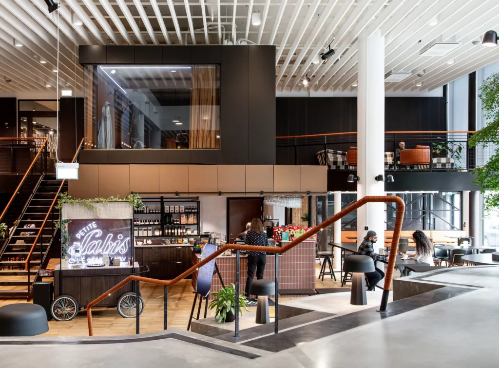 Ett modernt café med en öppen och ljus interiör, inkluderande en trätrappa, sittgrupper och en kaffebar med hyllor fyllda med produkter.